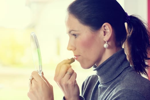 young dark haired woman looking in mirror and applying make up