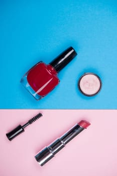 makeup collection with  mascara, nail polish ,eye shadow and brush from above on blue and pink ground