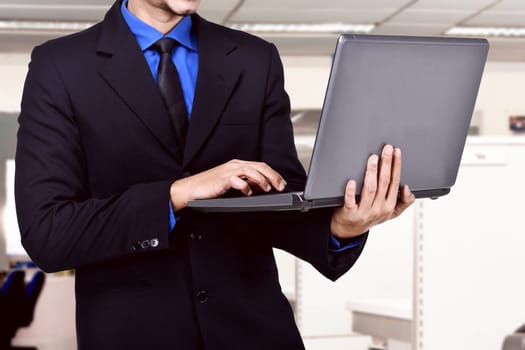 Businessman holding laptop while typing on the office