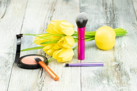 Decorative composition of various professional cosmetic brushes with a bouquet of yellow tulips. Presented on a rustic bright wooden table. Concept  greeting card design.