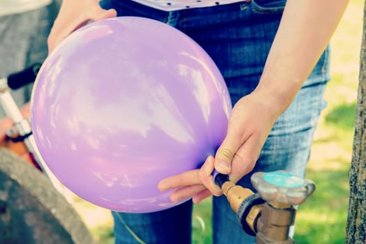 woman filling violet balloon with helium gas