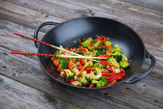 wok with colorful vegetables and chopsticks on wooden ground
