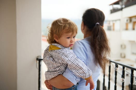 A loving mother holds her child while standing on a balcony, symbolizing warmth, care, and family togetherness in an urban setting.