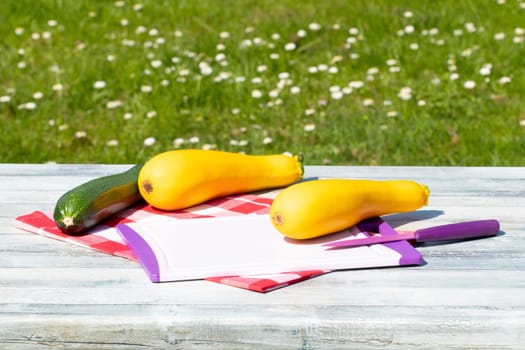 Two fresh yellow and one green courgette an cutting board with knife on rustic bright wooden table with natural green background. Concept health.