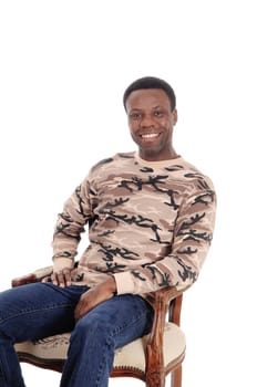 A smiling African American man in jeans and a sweater sitting .on chair looking into the camera, isolated for white background.