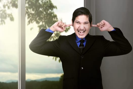 Unhappy asian businessman covering his ears to not hear great noise at home
