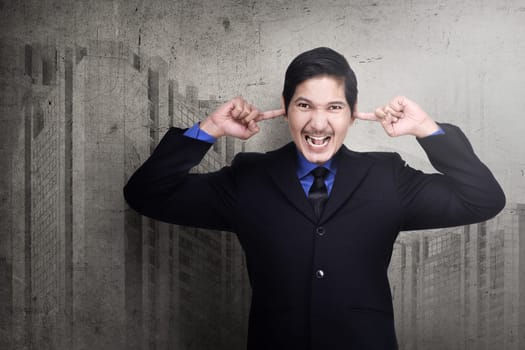 Stressed asian business man plugging his ears with fingers over abstract background