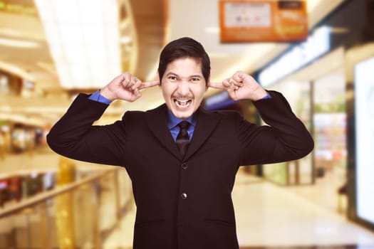 Young asian businessman covering ears with his finger on the mall