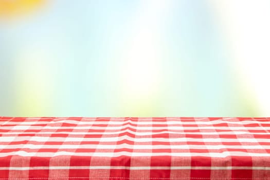 An empty table with a red checkered tablecloth and an pastel colorful natural background on a  sunny day. For your food and product display montage. Concept food.
