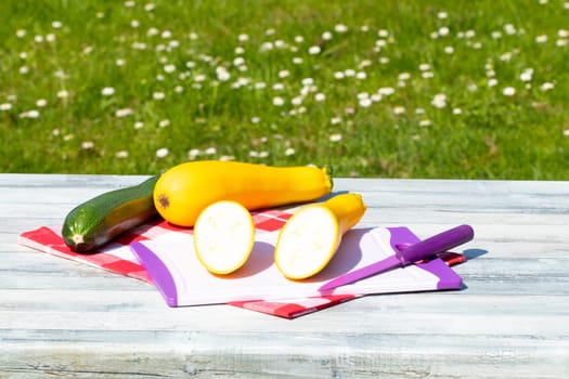 Three fresh courgette on rustic bright wooden table with natural green background. One of the yellow zucchini was freshly sliced on an cutting board. Concept health.