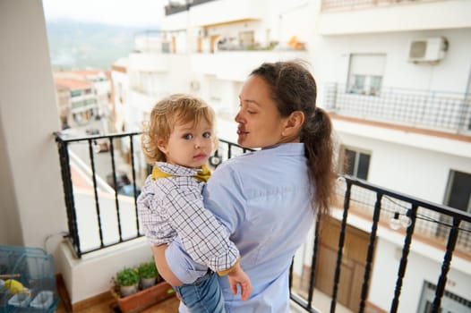 A mother joyfully spends time with her child on a balcony overlooking city buildings, embodying the love and connection shared between family members in a serene urban setting.