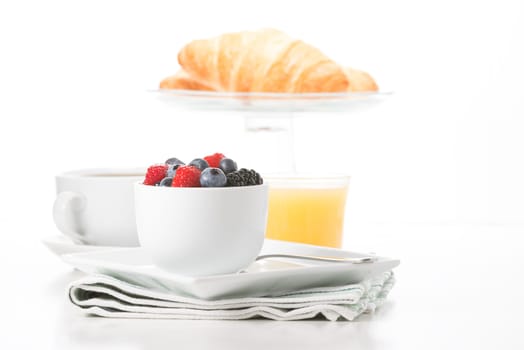 Small bowl of fresh berries served with croissant, coffee and orange juice.