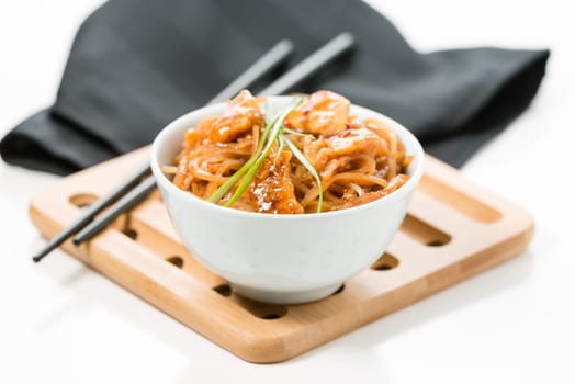 Spicy pad thai in a white bowl on a bamboo trivet.