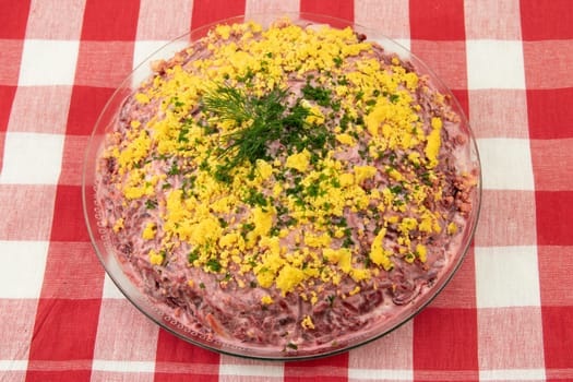 Traditional russian layered salad named herring under a fur coat. Traditional Russian cusine presented on red checkered tablecloth. Concept Russian food.