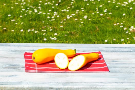 Two yellow fresh courgette on rustic bright wooden table with natural green background. One of the yellow zucchini was freshly sliced. Concept health.