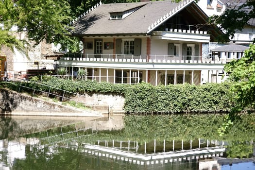 A residential building with a terrace is reflected on the banks of a river in the water.