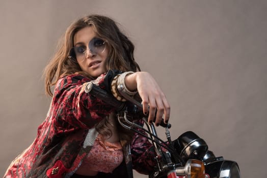 A sexy girl sit on a bike with hands on the handlebar long blonde hair and sunglass