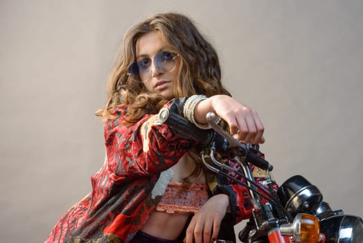A sexy girl sit on a bike with hands on the handlebar long blonde hair and sunglass