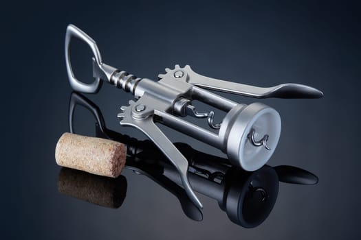 Steel corkscrew for wine and cork on a dark mirror background.