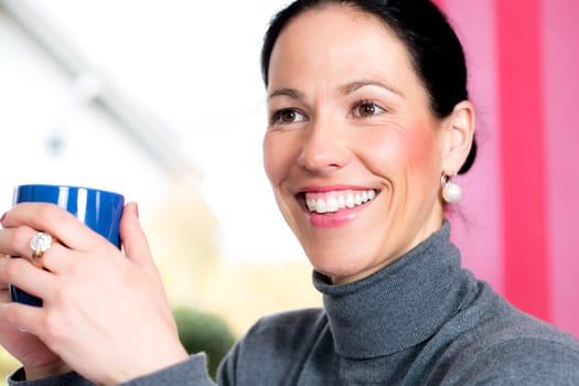 young dark haired woman at home with cup of coffeee is smiling