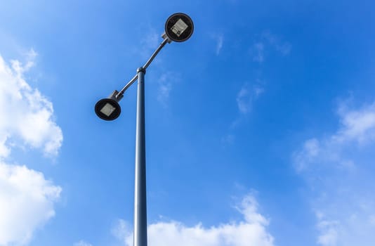 Modern electric street light pole over blue sky with clouds