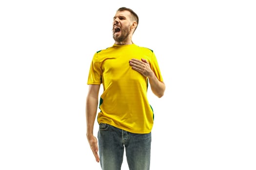 Brazilian fan celebrating on white background. The young man in soccer football uniform standing and singing a hymn at white studio. Fan, support concept. Human emotions concept.