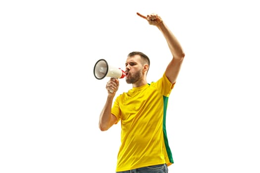 Brazilian fan celebrating on white background. The young man in soccer football uniform with megaphone at white studio. Fan, support, win, winner concept. Human emotions concepts.