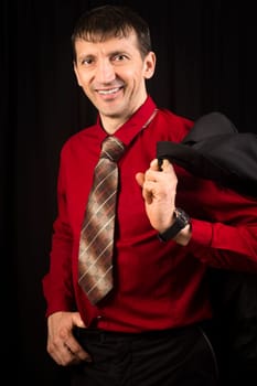 Elegant handsome smiling man is posing in red shirt and necktie on black background.