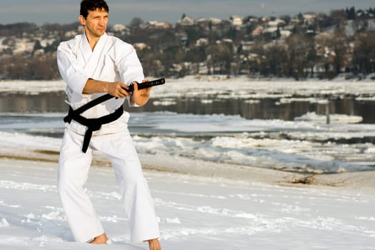 White ninja with sword is practicing martial arts on the snow at winter.