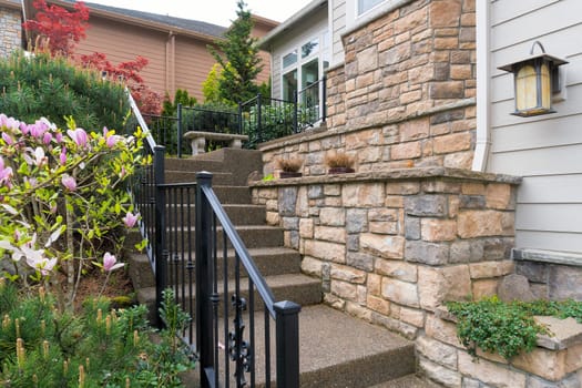 House front entry with concrete stairs iron rod railings stone wall planter siding by frontyard garden