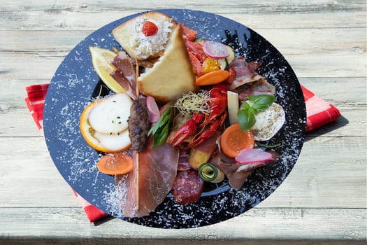Mixed typical Italian antipasto with ham vegetables and cancer. Concept traditional Italian food. Presented on rustic wooden table with red checkered tablecloth.
