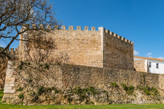 LAGOS, PORTUGAL - CIRCA MAY 2018: View of the entrance arch of the Governors Castle (Castelo dos Governadores) with palm trees in the foreground and tourists enjoying the setting, Lagos, Algarve, Portugal