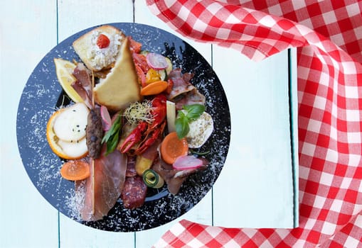 Mixed typical Italian antipasto with ham vegetables and cancer. Concept traditional Italian food. Presented on rustic wooden bright table with red checkered tablecloth.