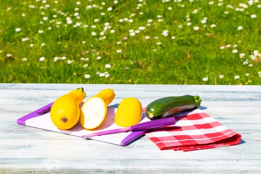 Three fresh courgette on rustic bright wooden table with natural green background. One of the yellow zucchini was freshly sliced on an cutting board. Concept health.