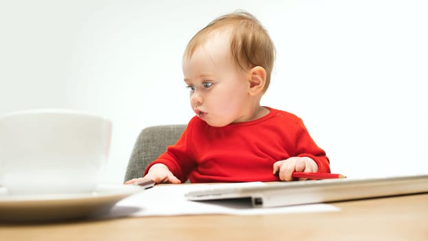 Happy child baby girl sitting with keyboard of modern computer or laptop isolated on a white studio background. early development of modern kids concept. Female caucasian up to a year old baby