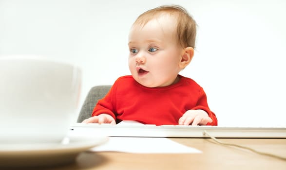 Happy child baby girl sitting with keyboard of modern computer or laptop isolated on a white studio background. early development of modern kids concept. Female caucasian up to a year old baby