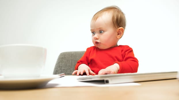 Happy child baby girl sitting with keyboard of modern computer or laptop isolated on a white studio background. early development of modern kids concept. Female caucasian up to a year old baby