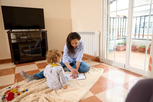 A loving mother spends quality time teaching her young child, fostering learning and bonding on a cozy blanket in a bright and warm home setting.