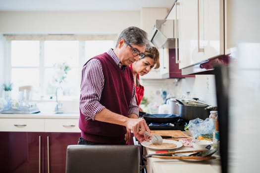 Mature couple are preparing a Pakistani meal at home. The man is cutting chapati and the woman is watching him closely.