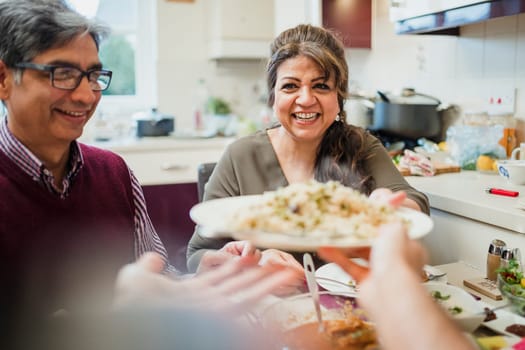 Point of view shot of a mature mother passing a serving of curry and rice to her son at the dining table.