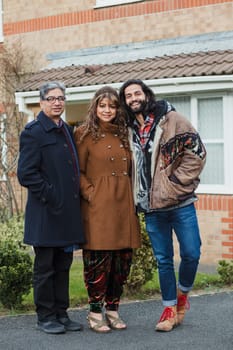 Portrait of a mother, father and mid adult son on the driveway of their home.