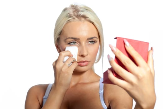Young woman clean face and eyes with wet wipes, holding mirror, remove make-up, body breast lingerie