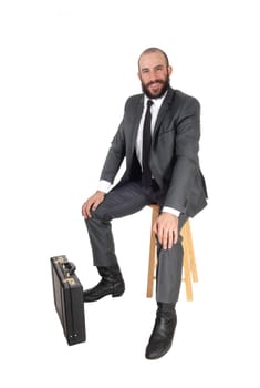 A young handsome business man wearing a suit and tie sitting.on a bar chair with his briefcase, isolated for white background.
