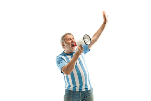 The senior Argentinean fan celebrating on white background. The mature man in soccer football uniform screaming in megaphone isolated at white studio. Fan, support concept. Human emotions concept.