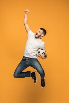 The young man as soccer football player jumping and kicking the ball at studio on a yellow background. Jumping footballer in a combat kick. Football fan and world championship concept. Human emotions