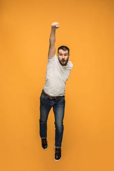 Freedom in moving. Mid-air shot of handsome happy young man jumping and gesturing against orange studio background. Runnin guy in motion or movement. Human emotions and facial expressions concept