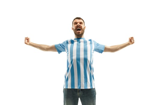 The young Argentinean fan celebrating on white background. The young man in soccer football uniform as winner isolated at white studio. Fan, support concept. Human emotions concept.