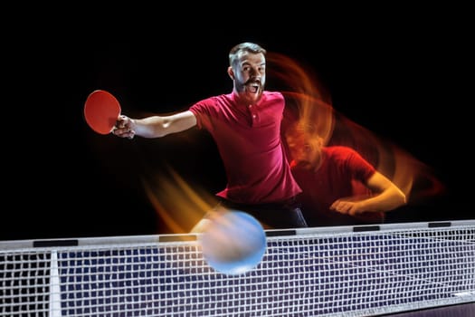The table tennis player in motion. Fit young sports man tennis-player in play on black background with lights. Movement, sport game, stobe concepts. Professional. Human emotions, facial expression