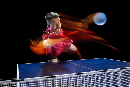 The table tennis player in motion. Fit young sports man tennis-player in play on black background with lights. Movement, sport game, stobe concepts. Professional. Human emotions, facial expression