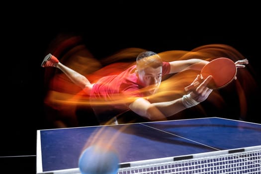The table tennis player in motion. Fit young sports man tennis-player in play on black background with lights. Movement, sport game, stobe concepts. Professional. Human emotions, facial expression